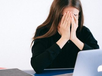 Woman covering face sitting in front of a computer